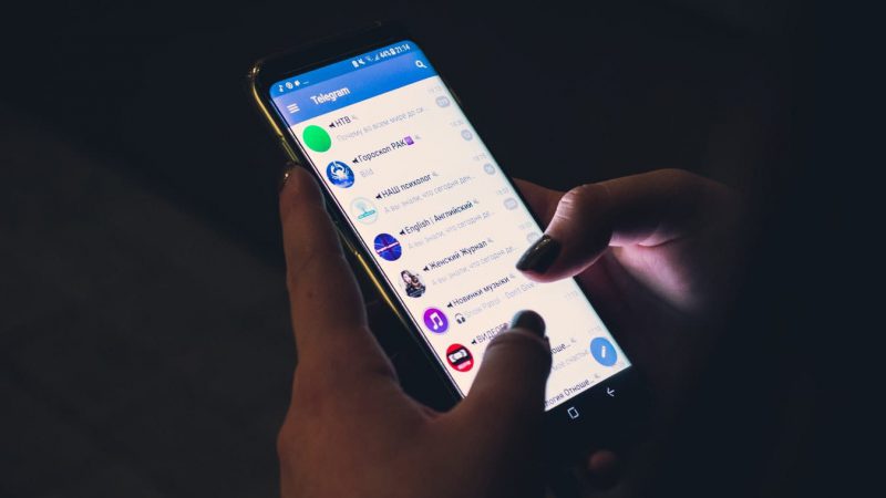 Een persoon die een smartphone vasthoudt met sociale media-iconen, waaronder Telegram.
